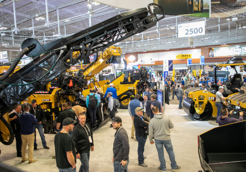 A group of people gathered around paving and construction machines at World of Asphalt.