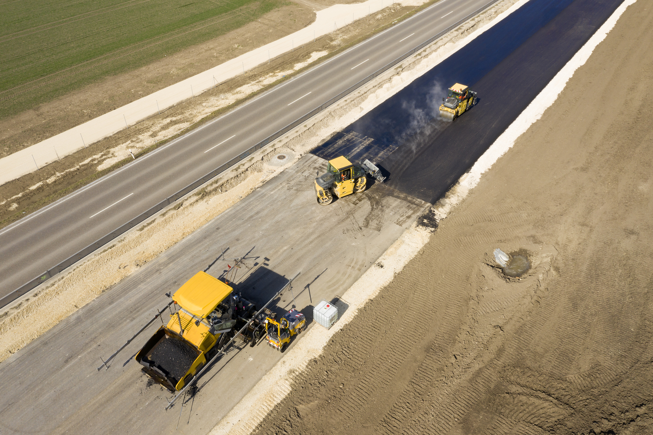 Aerial view of an asphalting paver machine and other construction machinery and vehicles during asphalting works on a new road.