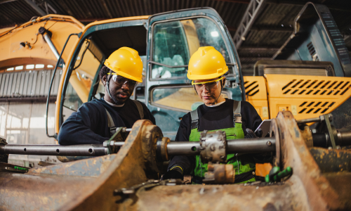 2 construction workers talking while working on equipment